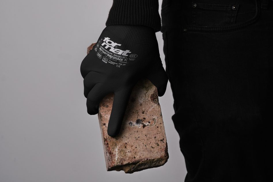 Close-up of a person wearing black gloves holding a brick. Perfect for mockups, templates, and construction-related design projects. High-resolution image for designers.