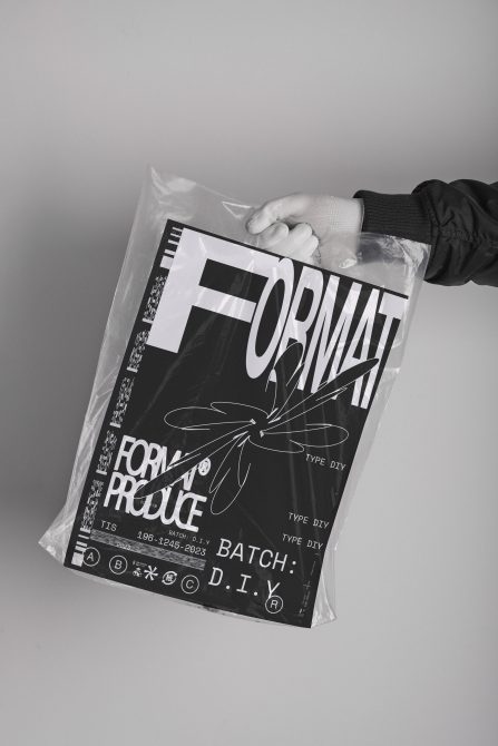 Black magazine wrapped in plastic held by gloved hands against gray background