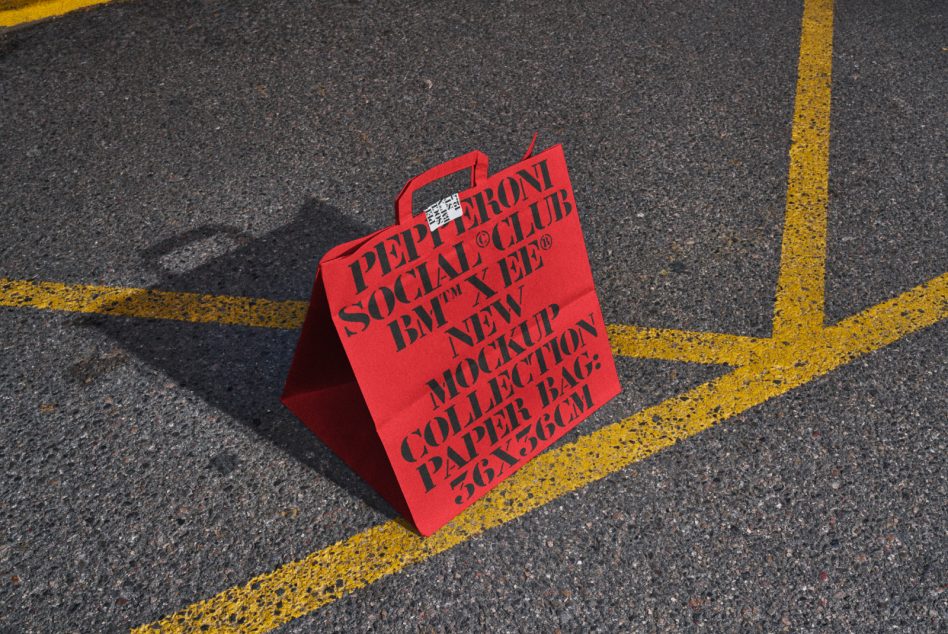 Mockup of a red paper bag with bold black typography on asphalt, perfect for designers. Keywords: mockup, paper bag, typography, graphic design, digital assets.