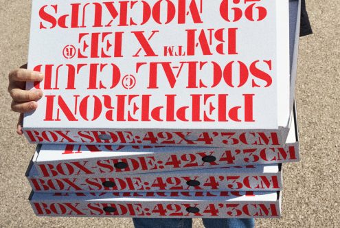 Person holding stacked pizza boxes with red stencil-style text, reading "BOX SIDE 42X43CM" and other words. Ideal for designers needing packaging mockups.