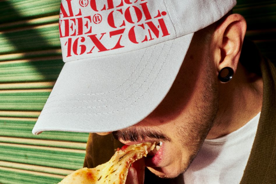 Man in white cap with red typography design, eating pizza. Ideal for fonts and graphics mockups, trendy urban fashion, food-related design templates.