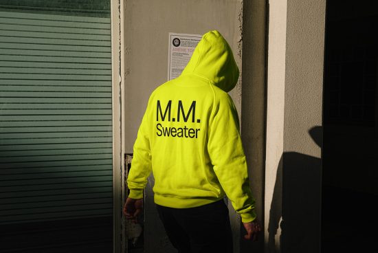 Man in neon green hoodie with M.M. Sweater text on the back standing near a wall, suitable for mockups, fashion design templates, marketing graphics.