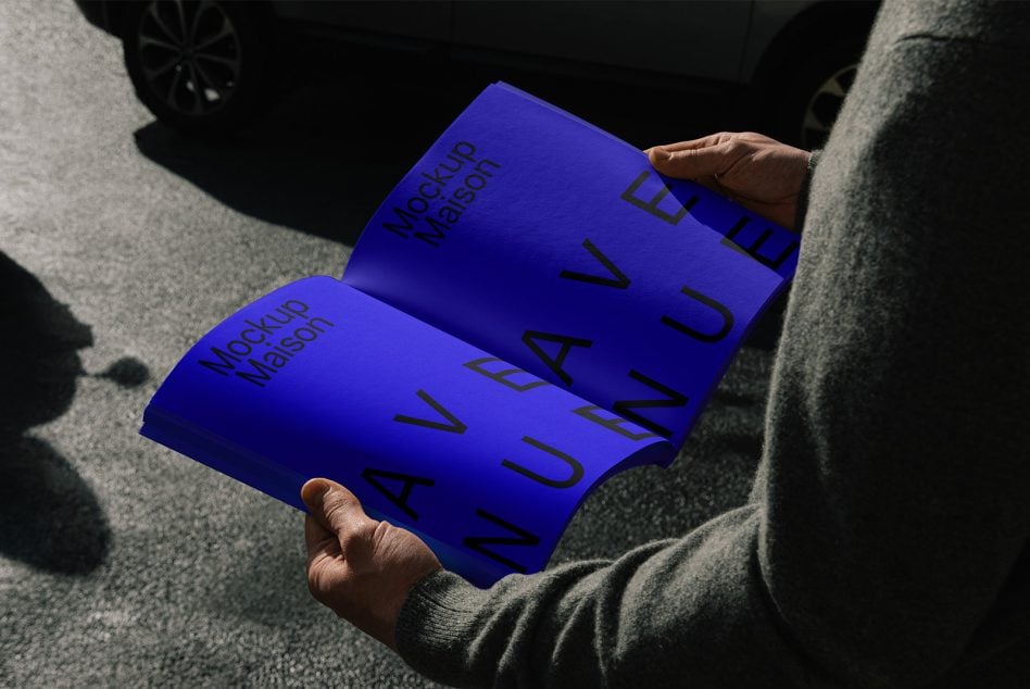 Hands holding open blue magazine mockup with Mockup Maison Avenue branding
