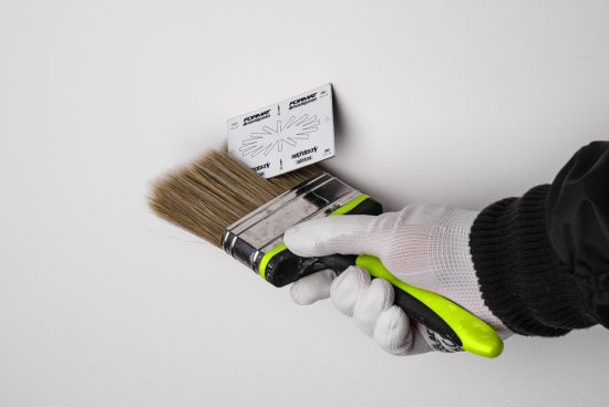 Hand holding green and black brush next to adhesive template on a white wall. Ideal for designers needing mockups, graphics tools, or wall paint templates.
