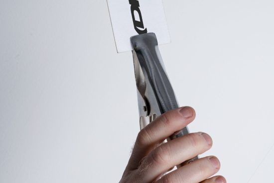 Closeup of hand holding metal clamp with attached printed card. Ideal for mockups, templates, and graphic design projects. High-resolution image.