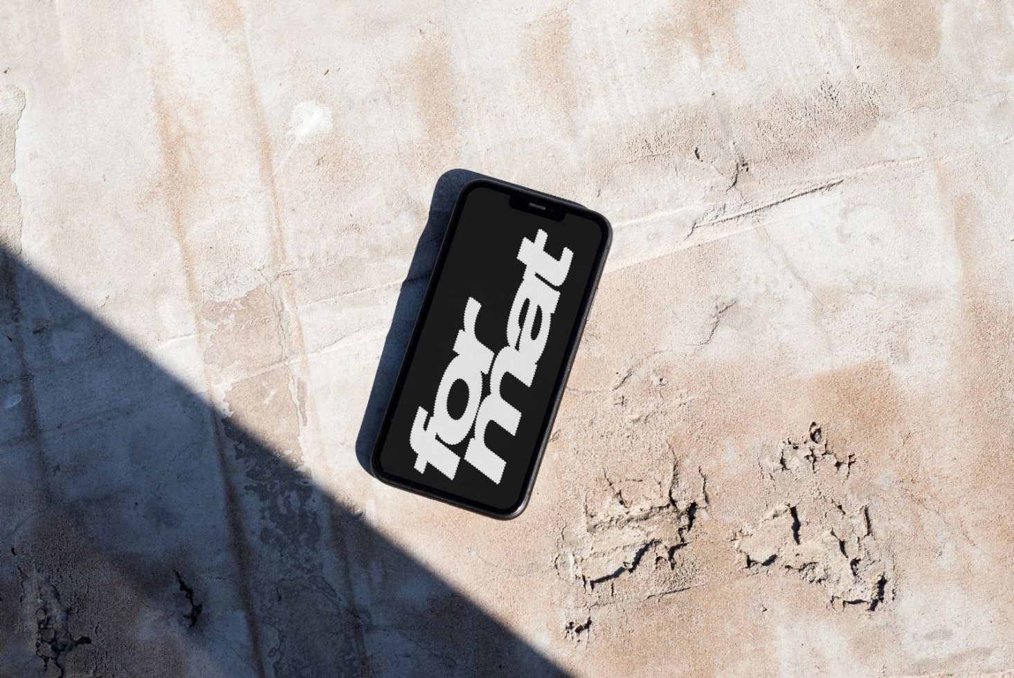 Phone screen displaying "format" on a concrete surface partially in shadow. Suitable for mockups, design templates, or graphic background assets for designers.