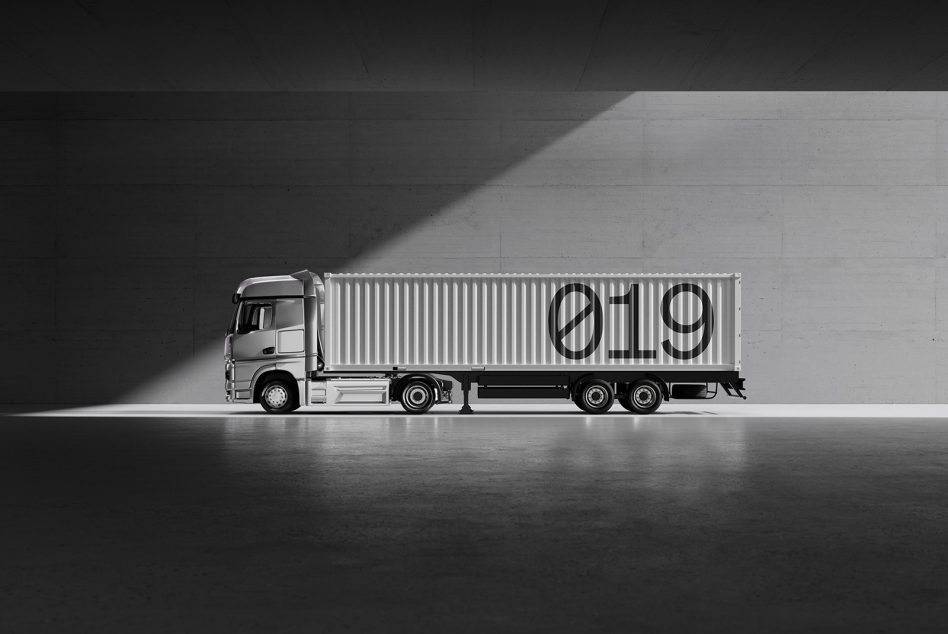 Black and white side view of a truck with a container featuring the number 019, casting shadows in a minimalist concrete setting, ideal for mockups and graphics.