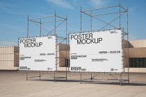 Two large posters on metal scaffolding against blue sky with industrial buildings behind