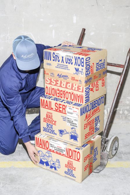 Courier in blue uniform handling stacked cardboard boxes labeled Mail Service using a hand truck in a warehouse environment. Packaging graphics and mockups