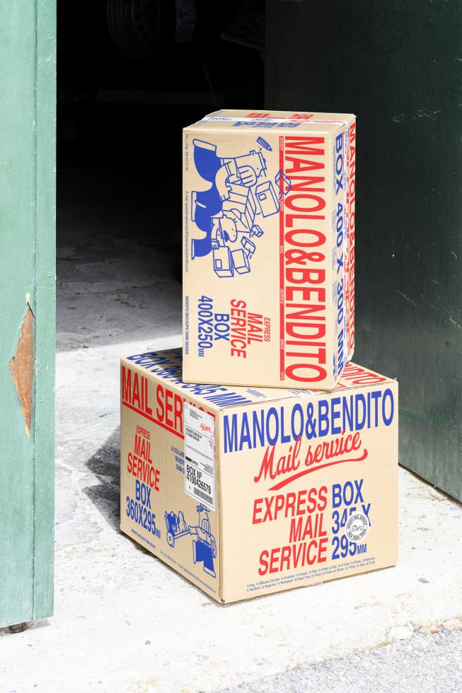 Two stacked cardboard boxes with colorful text and illustrations for mail service, captured outdoors near a green door; ideal for packaging and logistics mockups.