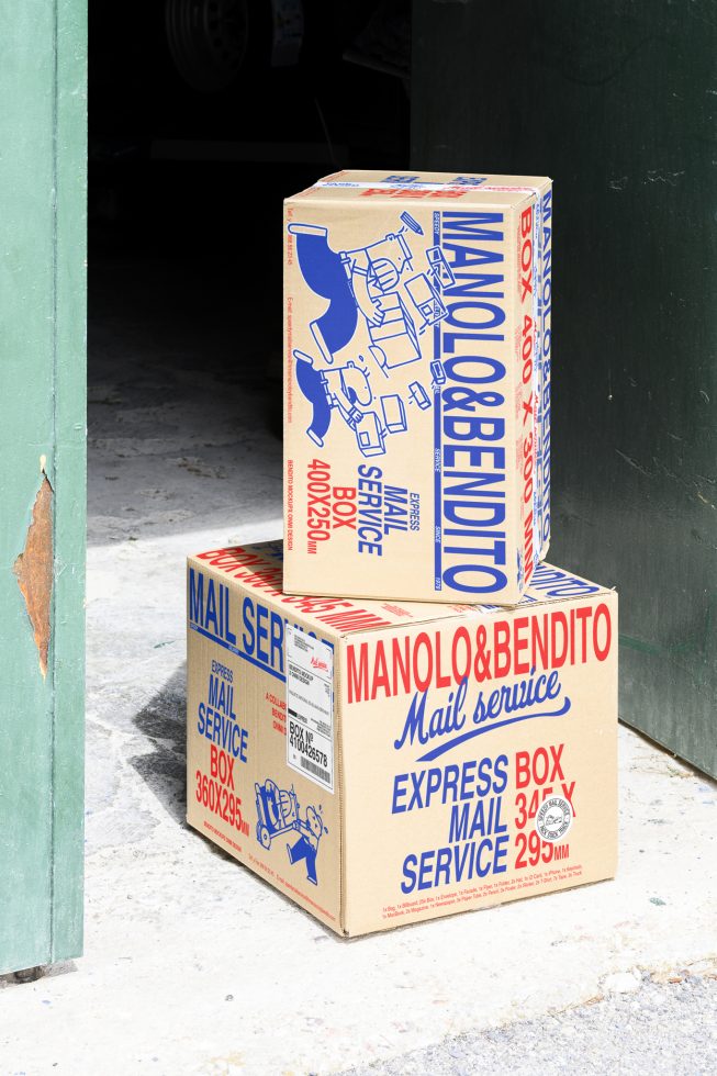 Cardboard boxes with blue and red typography design, labeled Manolo&Bendito Mail Service, suitable for packaging mockups for digital asset designers.