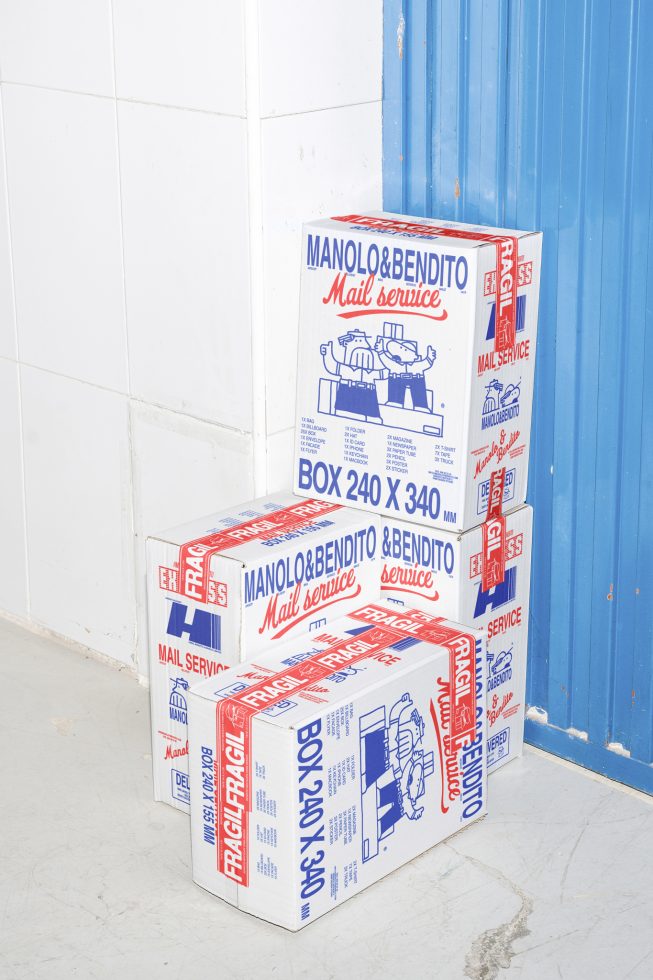 Stacked white cardboard boxes with Manolo&Bendito Mail Service branding, showing in a warehouse; packaging mockup, delivery design, shipping graphics.