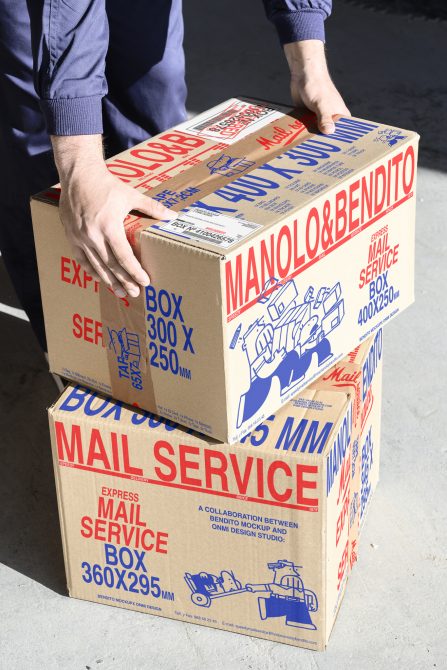 Hands holding two stacked cardboard boxes with bold red and blue graphics. Perfect for packaging mockups, ecommerce templates, shipping graphics.