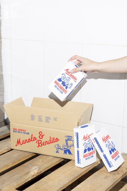 Hand placing small box into cardboard mailer with postal service branding