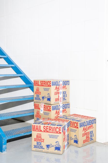 Stack of four vintage mail service boxes in a minimalist white room beside a blue staircase. Perfect for mockups, graphic design, branding, packaging.