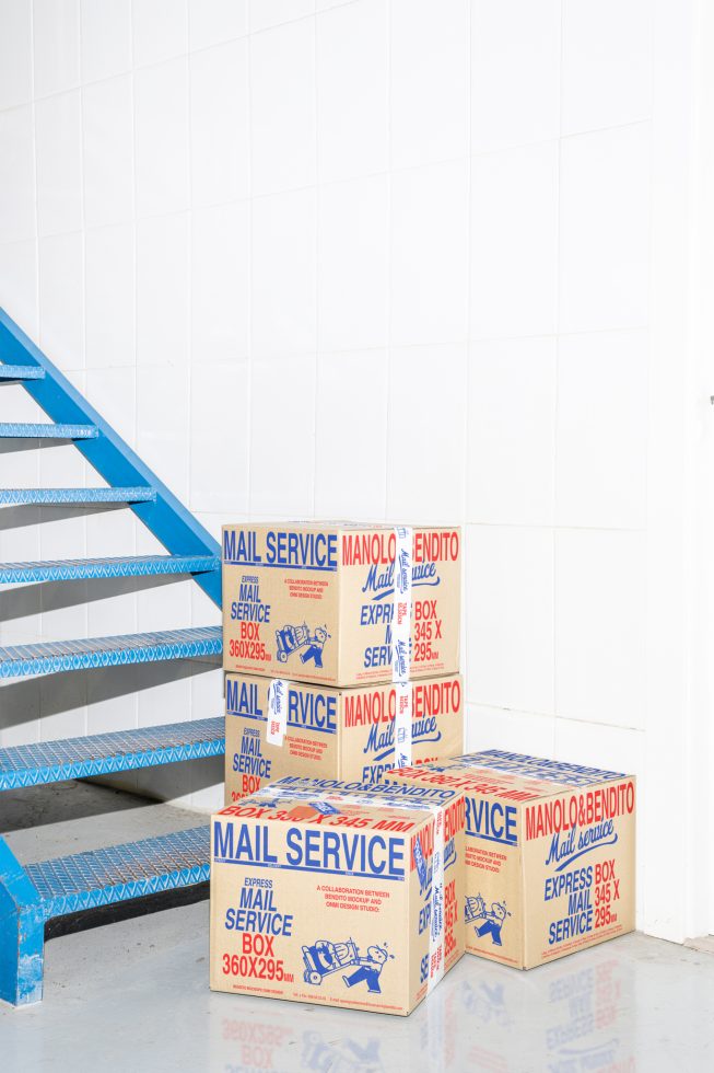 Cardboard mail service boxes stacked beside blue metal stairs in a white-tiled room. Ideal for packaging mockups, shipping graphics, and delivery design templates.