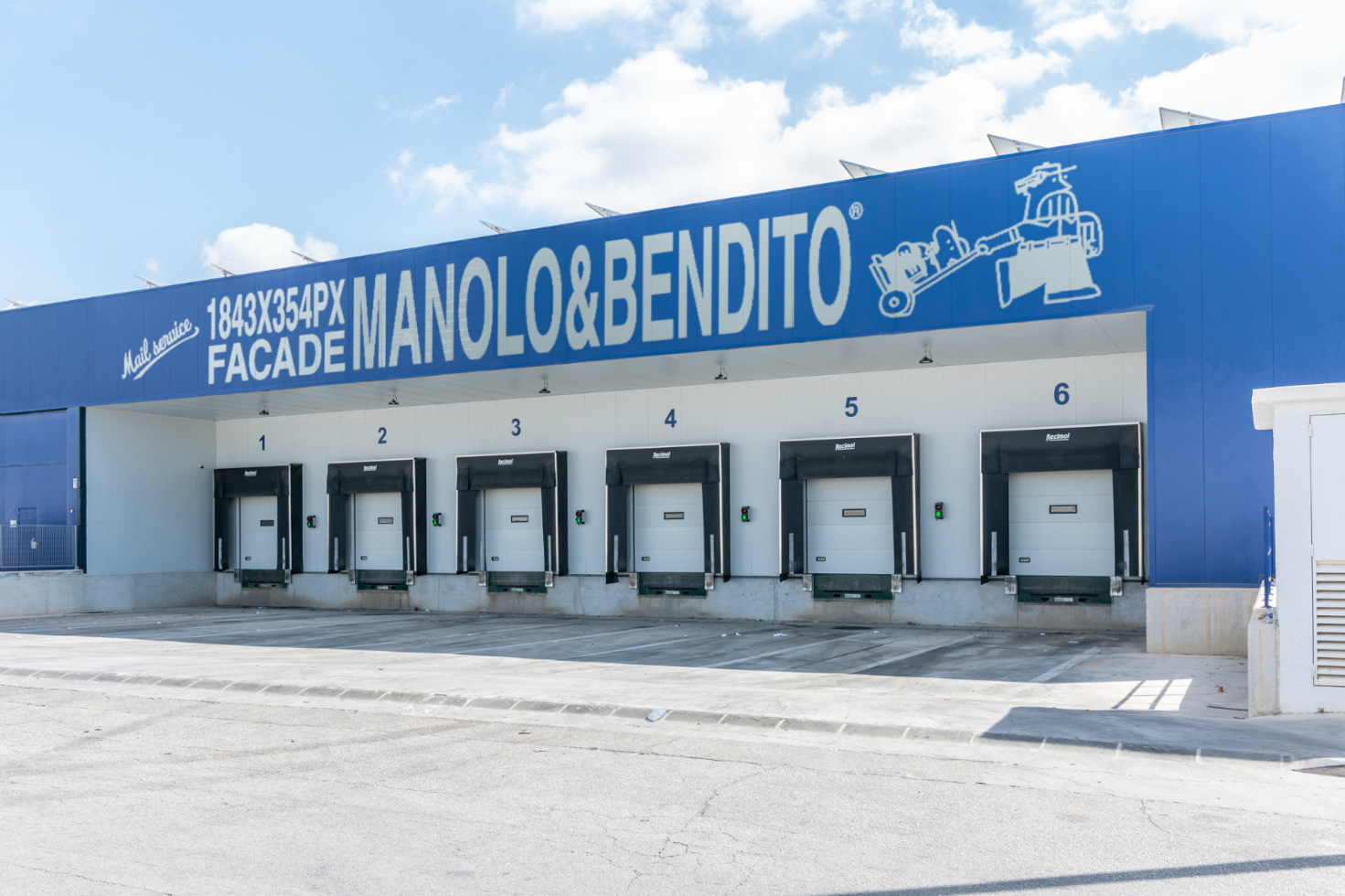 Factory facade with six loading docks and a blue banner displaying text Manolo Bendito. Suitable for mockup designs. Industrial, warehouse, logistics.