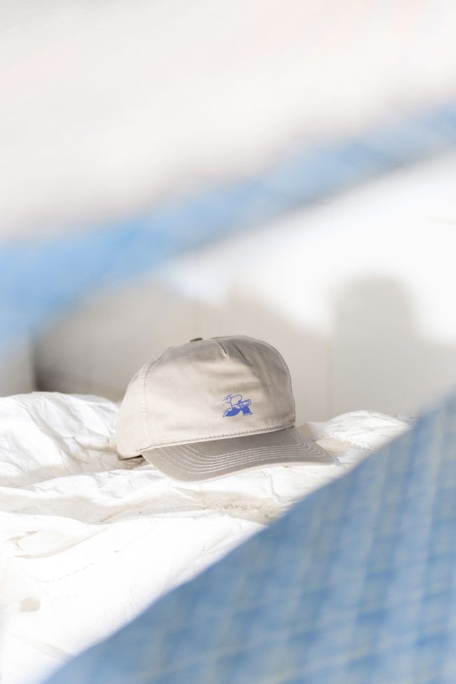 Beige cap mockup with blue logo placed on crumpled white fabric, perfect for designers showcasing branding and apparel design. High-resolution graphics.