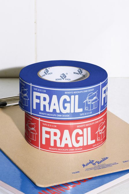 Stacked rolls of Fragile tape mockup in blue and red colors on a desk. Perfect for packaging, branding design, and graphic design projects for designers.