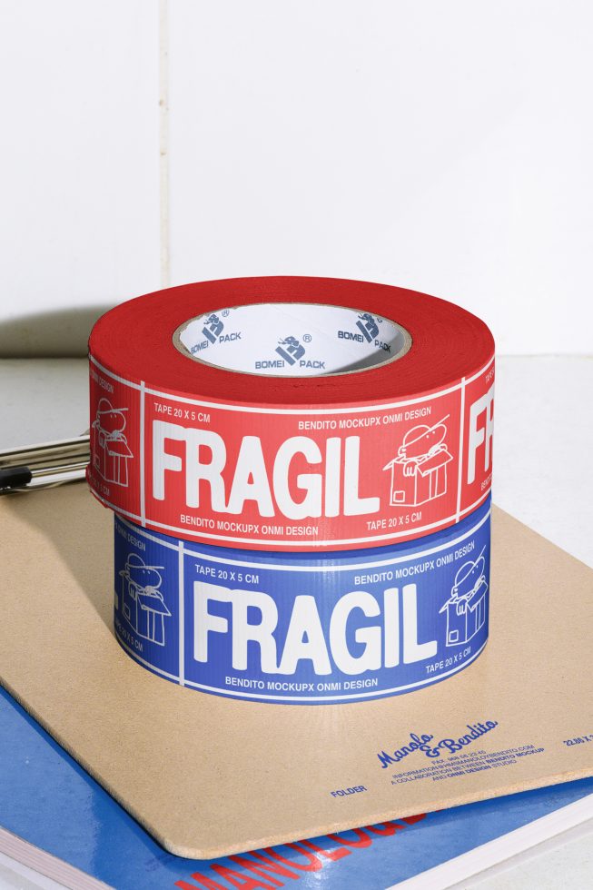 Mockup of red and blue fragile packing tape with printed text and icons for packaging design projects on a tabletop. Keywords: Mockups, Packaging, Design resources.