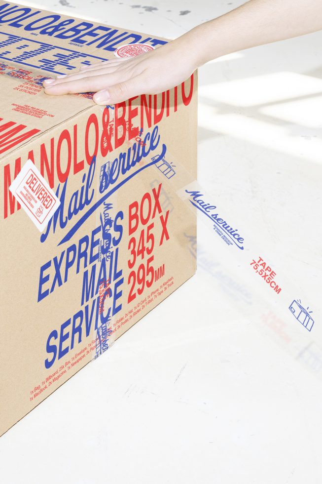 Cardboard box mockup with blue and red typography for mail service Manolo&Bendito. Features delivered sticker and clear tape. Ideal for packaging design projects.