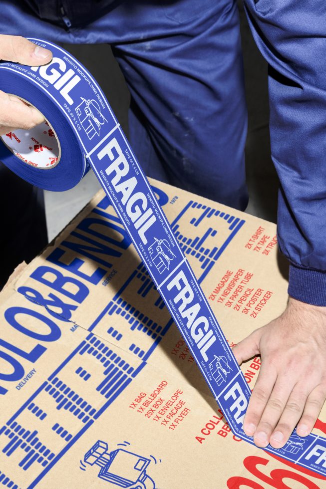 Person sealing cardboard box with blue fragile tape suitable for shipping and packaging mockups featuring bold labels and industrial design elements