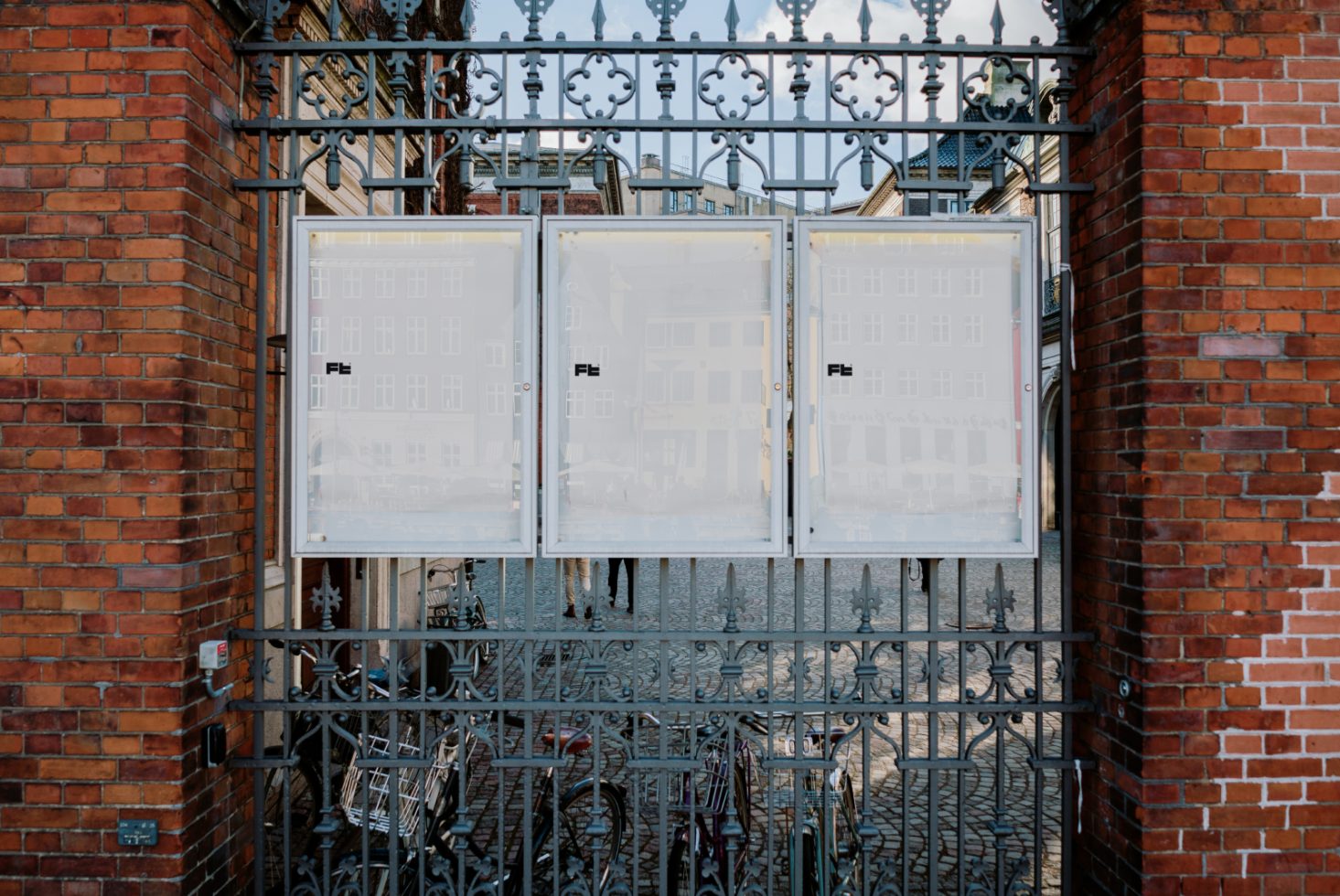 Iron gate in city setting featuring three blank posters mounted on it surrounded by red brickwork useful for street mockup templates urban design concepts.