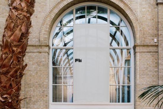 Arched window with a white banner mockup, surrounded by brick walls and tropical plants in an architectural setting, ideal for design presentations.