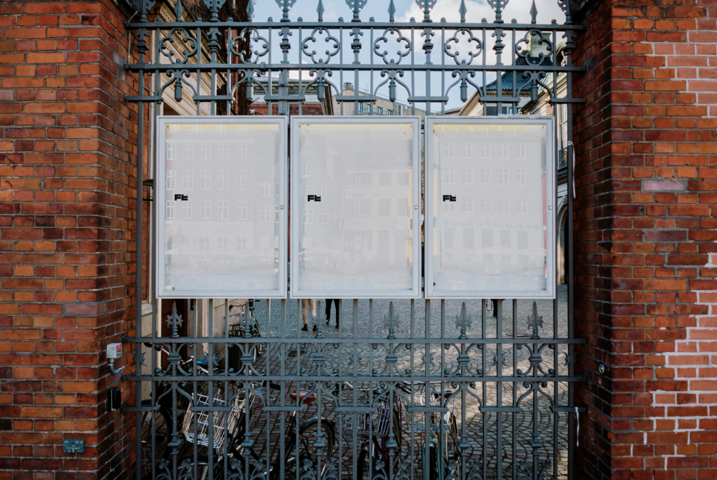 Iron gate with three vertical blank poster mockups for street advertising in urban setting between brick pillars perfect for designers' presentation background