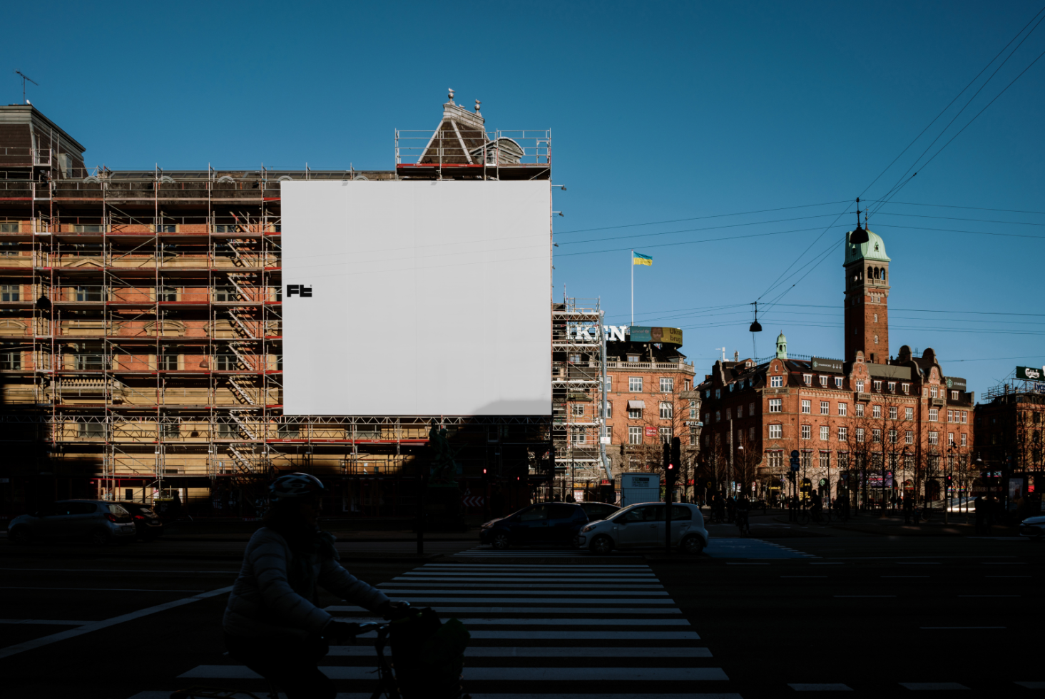 Blank billboard mockup on a scaffolding-covered building in a cityscape with cyclists and cars. Ideal for advertising, urban design, and promotional templates.