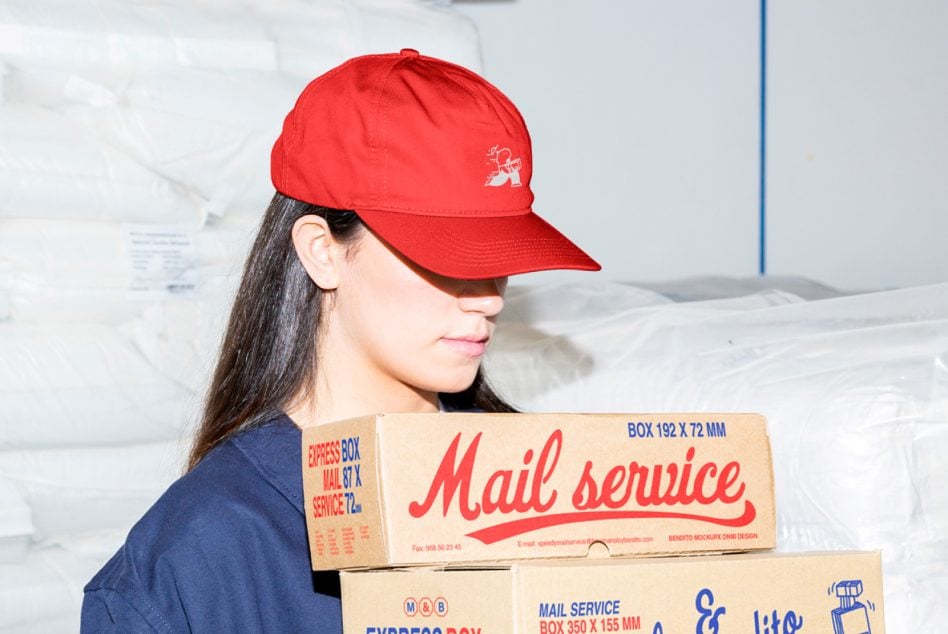 Woman in red cap holding stacked cardboard boxes with Mail service branding