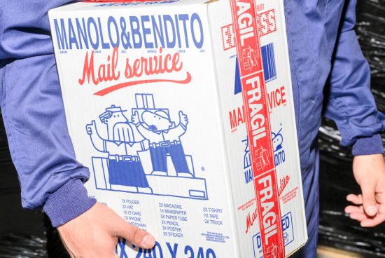 Close-up of a person in a blue uniform holding a white cardboard box labeled Manolo and Bendito Mail Service with red Fragile tape.