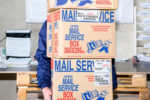 High-quality mockup featuring a person holding three stacked mail service boxes in a postal setting ideal for graphic designers looking for realistic packaging templates.