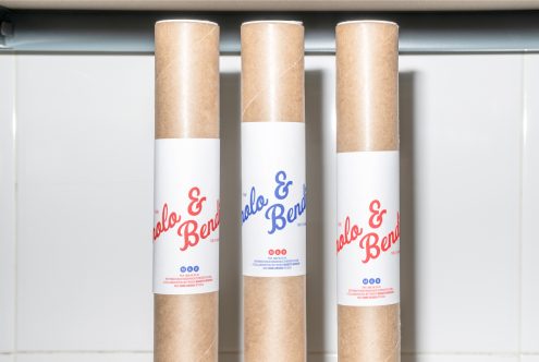 Three brown cardboard tube mockups with white labels displaying the text Polo & Bendo in red and blue, standing upright on a white tiled background.