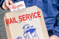 Hand holding kraft envelope with red "Mail Service" branding, blue delivery illustrations, white business card peeking out
