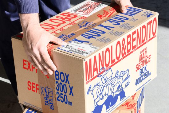 Person handling a cardboard shipping box with text MANOLO & BENDITO. Ideal for packaging mockup designs. Keywords: shipping, box, packaging, design, mockup.