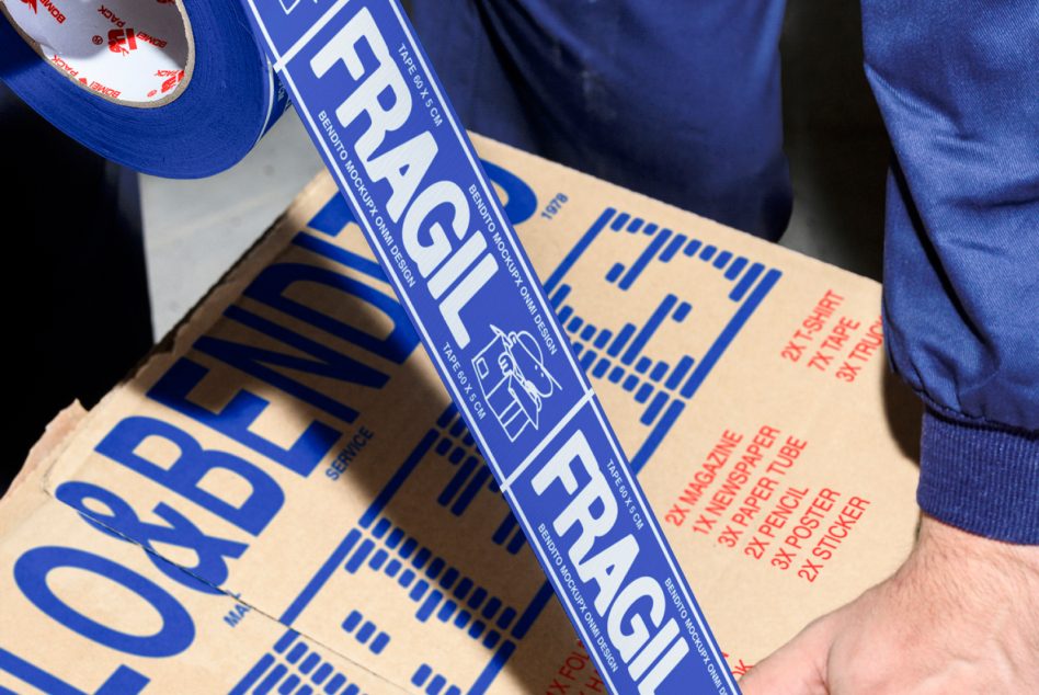 Blue tape with fragile text on cardboard box; packaging mockup for designers. Designer putting tape on moving box labeled fragile. Mockups, Graphics, Templates.