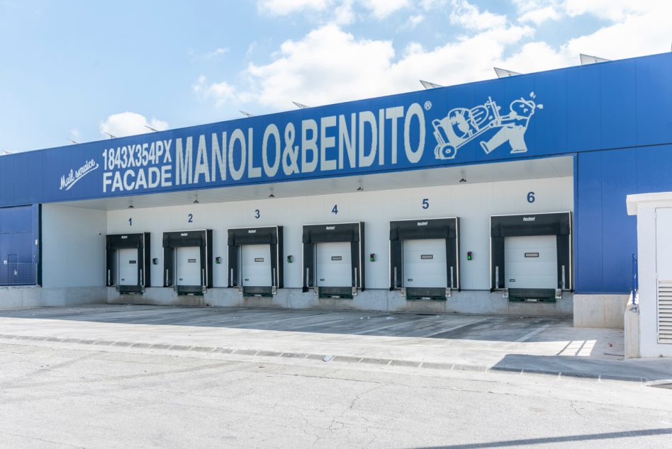 Industrial warehouse loading dock with bright blue signage, numbered bay doors, clear sky