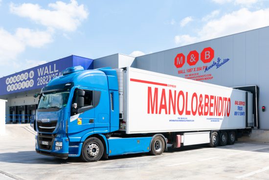 Blue truck with Manolo and Bendito logo parked at a warehouse with signage. Ideal for delivery, logistics mockup templates. Premium design asset for designers.