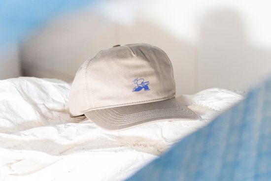 Tan baseball cap with blue running cartoon graphic. Cap resting on white fabric, blurred background. Perfect for apparel mockup, product photography, branding design.