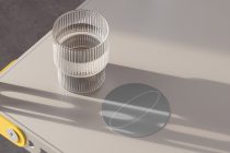 Transparent striped cylinder container next to circular coaster with minimalist oval graphic