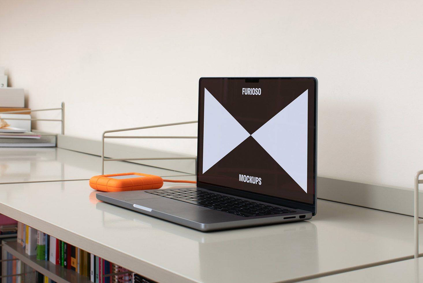 Laptop displaying screen mockup on a minimalistic desk with orange external hard drive and books in the background ideal for designers and digital assets.