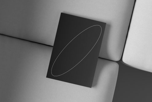 Black book cover mockup with a minimalistic design featuring a single oval line, placed on a grey cushioned surface. Keywords: book mockup, minimal design.