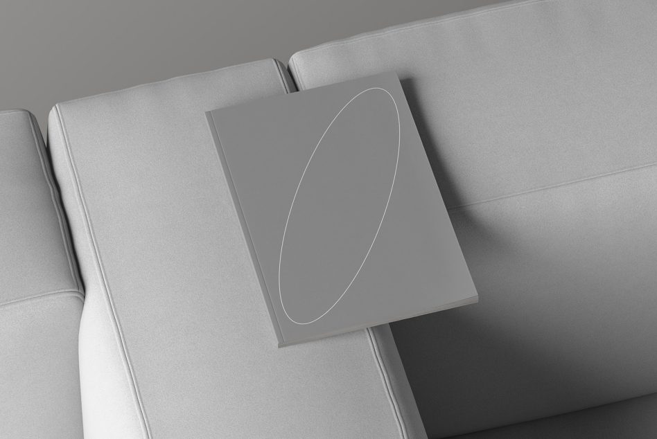 Magazine mockup with a minimalist cover design showcasing an oval shape displayed on a modern grey sofa perfect for print templates and graphic design presentations