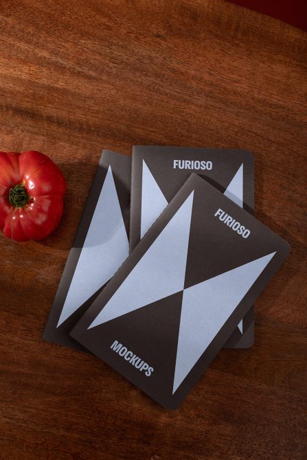 Stack of three mockup templates on a wooden surface with a red tomato. Ideal for design presentations. Keywords: mockups, templates, designer resources.