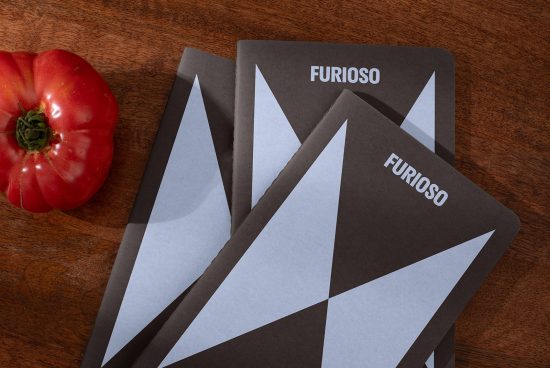 Set of three geometric pattern notebooks titled Furioso beside a ripe red tomato on wooden surface Keywords: mockups design templates designers stationery