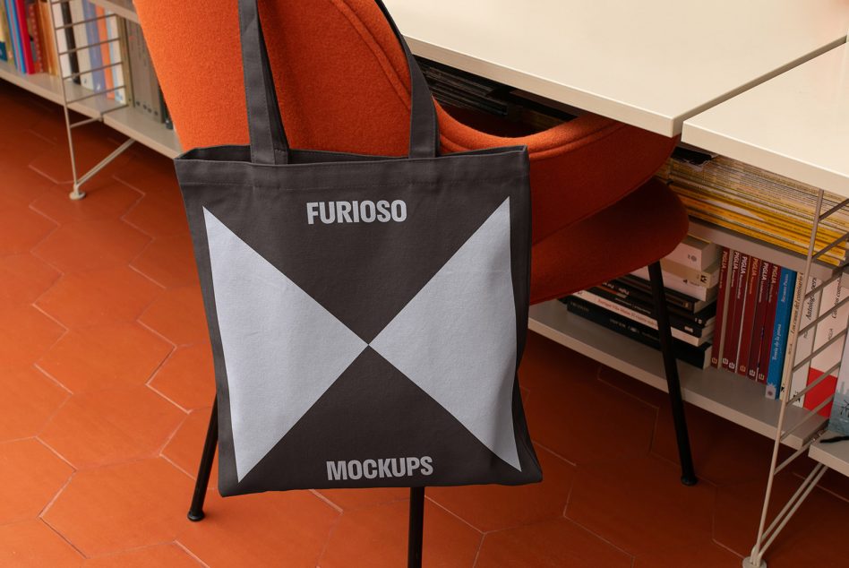 Tote bag mockup hanging on chair in home office setting with bookshelf and orange chair stylish digital asset for designers keywords tote bag mockup designers