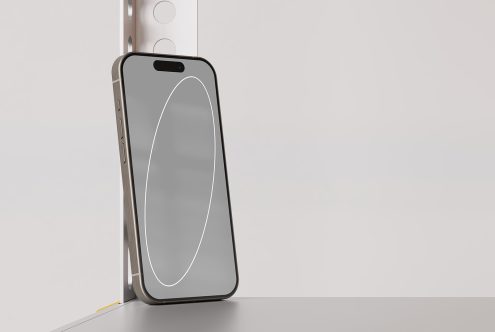 Mockup of a modern smartphone standing against a metal structure on a grey surface with a minimalistic white background. Keywords: mockup, smartphone, modern, minimalistic.