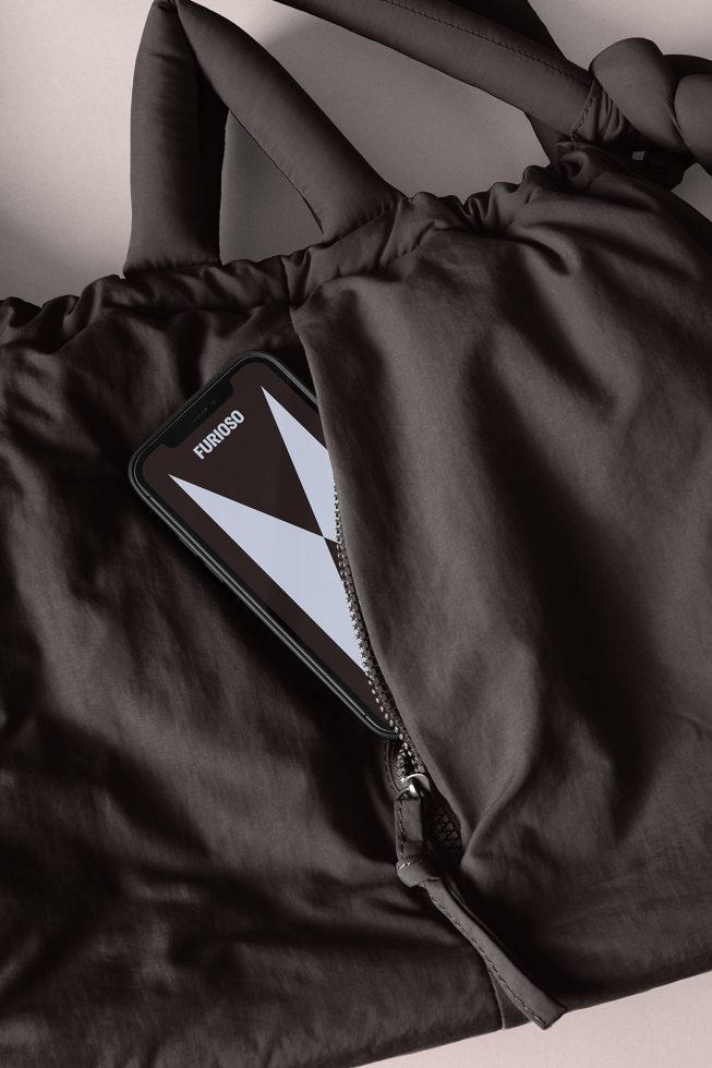 Minimalist tote bag mockup with a black smartphone featuring modern geometric graphics partially visible from the open zipper. Ideal for designers.