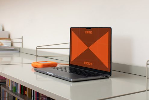 Laptop and orange external hard drive on a minimalist desk with books; perfect for showcasing digital mockups, templates, graphics in creative design projects.